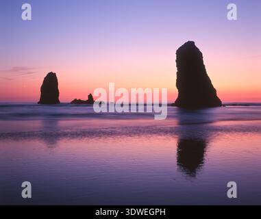 Gli Needles si stagliano sullo sfondo di un cielo colorato al tramonto a Cannon Beach, sulla costa dell'Oregon Foto Stock