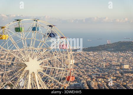 Una ruota panoramica si erge in alto contro le sfumature dorate del tramonto, affacciata sull'esteso paesaggio urbano di Barcellona dalle alture del Tibidabo, offrendo Foto Stock