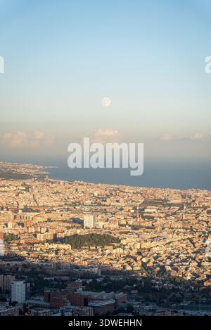 Splendida vista aerea di Barcellona da Tibidabo mentre il sole tramonta, illuminando il paesaggio urbano con un caldo bagliore. Il mare e l'orizzonte distante migliorano il Foto Stock