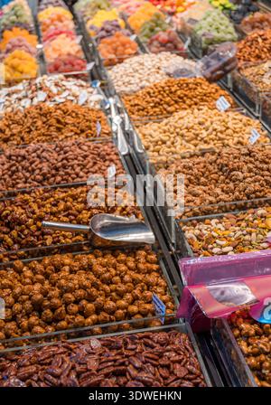 Una variopinta gamma di frutta secca, noci e spuntini ordinatamente disposti in un'esposizione al mercato. Un motivo armonioso sfoggia texture e colori diversi. Foto Stock