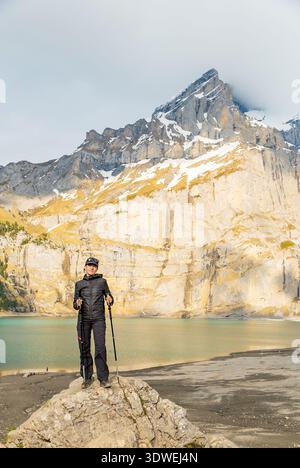Un escursionista si erge serenamente accanto alle acque turchesi del lago Oeschinen, annidato nelle maestose Alpi svizzere. Le cime innevate si innalzano maestosamente sul retro Foto Stock
