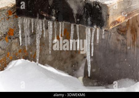 Primo piano di ghiaccioli appesi a una trave di legno, con la neve sottostante a Schonbiel, Zermatt, che mostra il fascino invernale del Vallese, l'alpin della Svizzera Foto Stock