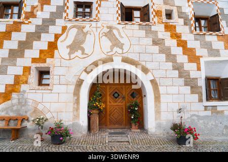 Incantevole architettura tradizionale di Scuol, un pittoresco villaggio annidato nelle Alpi svizzere. La facciata in pietra e i vibranti fiori aggiungono fascino e stile Foto Stock