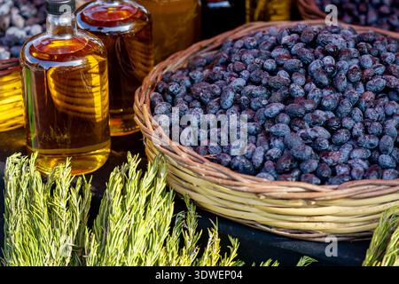 Un cesto pieno di urma vibrante si trova accanto a bottiglie di olio e rosmarino fresco. Questa composizione cattura l'essenza dei sapori mediterranei e. Foto Stock