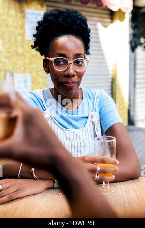 Una coppia condivide un piacevole momento mattutino mentre si gusta una colazione informale all'aperto. L'allegra signora è seduta ad un tavolo di legno e condivide un drink con spirito Foto Stock