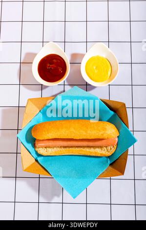 Un delizioso hot dog servito in un panino su un tavolo a scacchi. Accompagnato da due camamolini ripieni di ketchup e senape, che aggiungono sapore a questa classica S Foto Stock
