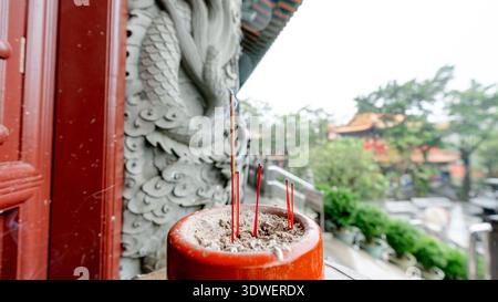 Primo piano di bastoncini di incenso che bruciano in una pentola al monastero di po Lin sull'isola di Lantau. Il fumo sorge dolcemente sullo sfondo di un'architettura tradizionale Foto Stock