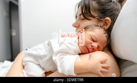 Un neonato riposa tranquillamente sul petto della madre in una stanza d'ospedale. Il momento di serenità cattura il calore e il legame condivisi tra madre e bambino Foto Stock
