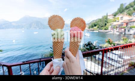 Gustando i vivaci coni di gelato verdi e rosa con biscotti a base di waffle, affacciati sulla bellezza panoramica del lago di Como, situato nell'affascinante città di Varenna, Foto Stock