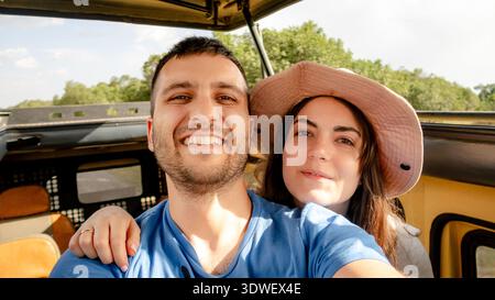 Una coppia felice scatta un selfie durante un avventuroso safari nella riserva Ol Pejeta del Kenya. Circondati da paesaggi lussureggianti, abbracciano il brivido Foto Stock