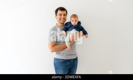 Un padre gioioso che tiene in braccio il suo bambino di cinque mesi, entrambi sorrisi di calore e connessione. Il bambino è vestito con un abbigliamento intimo, che incarna il puro f Foto Stock