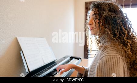 Una giovane donna suona con grazia il pianoforte, avvolto dalla luce naturale che scorre attraverso la finestra, catturando un momento musicale sereno e intimo in una Foto Stock