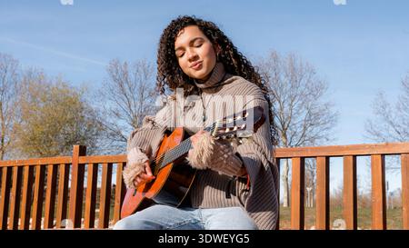 Una giovane donna ama suonare la chitarra all'aperto, mostrando la sua passione per la musica e la creatività in natura. Foto Stock