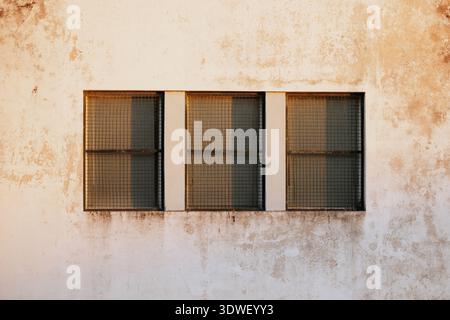Una facciata di un edificio d'epoca caratterizzata da tre finestre barrate su una parete rustica e intemprata. La texture antica e l'illuminazione naturale creano un nostalgico e un suo Foto Stock