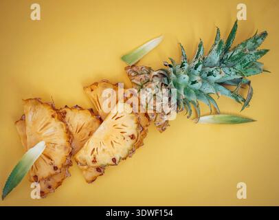 Fette di ananas fresche disposte ordinatamente su un vibrante sfondo giallo, che mostrano la succosa consistenza tropicale e le foglie di verde brillante di questo deliciou Foto Stock