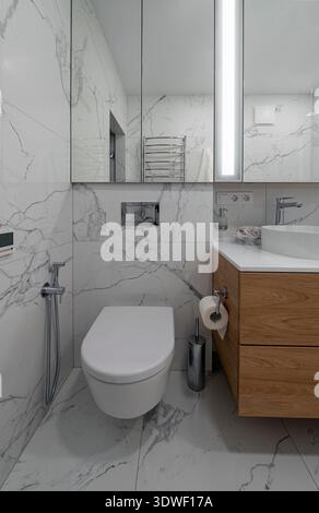 Un bagno moderno con eleganti pareti e pavimenti in marmo, completato da un elegante lavandino in legno. Lo spazio è dotato di attrezzature moderne Foto Stock
