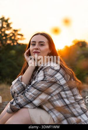 Una scena serena di una donna che si crogiola nel caldo bagliore di un tramonto estivo, con una luce soffusa che mette in risalto la sua espressione rilassata sullo sfondo di un vibra Foto Stock