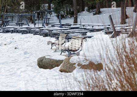 Panche e tavoli in legno ricoperti di neve in una terrazza all'aperto vuota presso una foresta durante la stagione invernale. Foto Stock