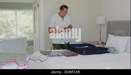 Impacchettare un uomo cinese maturo in camicia a righe sistemando valigia aperta in camera da letto, con passaporto in mano Foto Stock