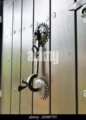 Primo piano di una maniglia per porta in ferro d'epoca e rosette decorative montate su una porta in legno verniciato, che mette in risalto la lavorazione in metallo rustico, la consistenza e lo stile Foto Stock