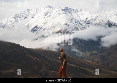 Un uomo guarda i paesaggi del Kirghizistan, viaggiando attraverso l'Asia centrale. Le montagne innevate si innalzano sopra valli nebbiose, creando un ambiente sereno e indimenticabile Foto Stock