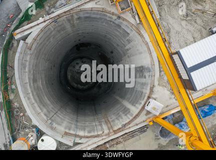 Veduta aerea di un enorme tunnel di costruzione, che mostra il suo profondo albero circolare con macchinari pesanti circostanti e attrezzature da costruzione presso il si Foto Stock