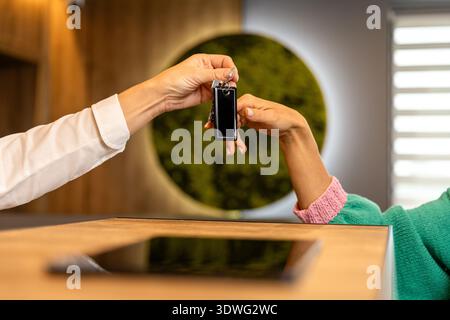 Il receptionist dà agli ospiti la chiave della camera durante il check-in presso il moderno banco ricevimento Foto Stock
