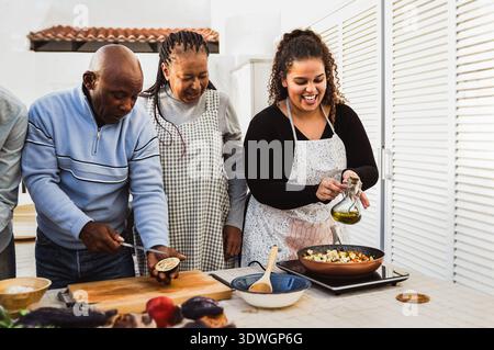 Famiglia africana felice che prepara insieme pasti vegetariani nel patio di casa - cucina all'aperto e concetto di legame familiare Foto Stock