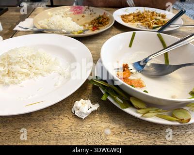 I piatti sporchi con i residui di cibo e riso sono collocati su un tavolo di legno, con utensili usati e un tovagliolo che suggeriscono un pasto finito Foto Stock
