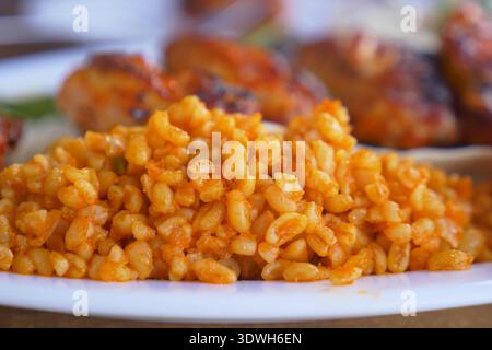 il riso bulgur si trova su un piatto bianco accanto alla carne e alle verdure grigliate Foto Stock