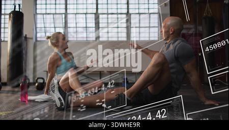 Donna e uomo seduti in un abbigliamento sportivo che condividono le metriche sul pavimento della palestra, sovrapposizioni AR Foto Stock