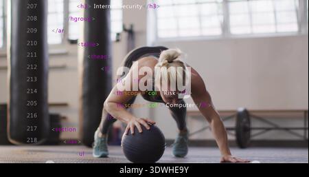 Equilibrio donna di mezza età con una sola mano su palla medica nera in palestra, reggiseno sportivo scuro Foto Stock