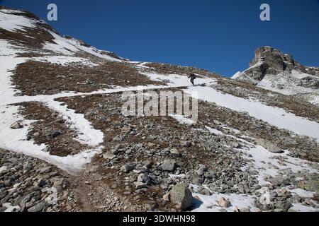 Escursionista che scende da un sentiero di switchback innevato dal passo Meidpass verso Gruben, Svizzera. Foto Stock