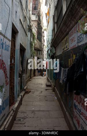 Uno stretto vicolo a Varanasi, India, con abiti appesi alle pareti e cartelli dipinti sugli edifici. Foto Stock