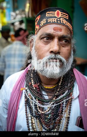 Primo piano di un uomo sacro barbuto adornato da numerose perle di preghiera e un cerchietto religioso a Varanasi, in India. Foto Stock