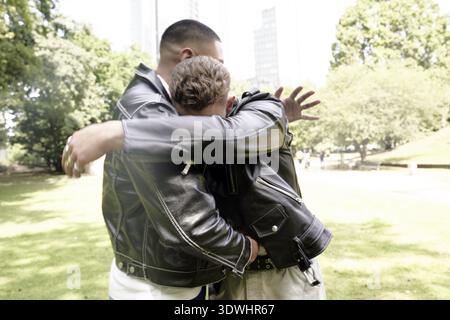 Incontro e saluto, due giovani uomini in un abbraccio di cuore in un parco all'aperto, amicizia, forte legame, amici, supporto, contare l'uno sull'altro, fiducia, Foto Stock