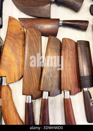 Coltelli da cucina in legno lavorati a mano disposti su una superficie neutra, con lame di diverse forme e impugnature dal design intricato, che enfatizzano la qualità della grana Foto Stock