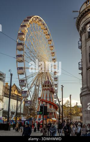 Fiera di Natale di Manchester, Cross Street, un giro su una grande ruota e giostra con folle di acquirenti nella calda luce della sera. Foto Stock
