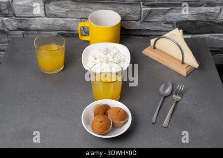 Succo d'arancia, caffè, muffin e formaggio fresco sul tavolo contro la pietra grigia Foto Stock