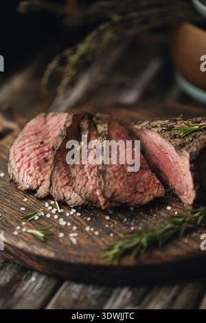 Succosa bistecca media di manzo Rib Eye fettine su tavola di legno con erbe, spezie e sale. Bistecca pronta da mangiare con ingredienti su un tagliere Foto Stock