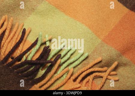 Soffice e calda coperta di lana d'alpaca con frangia. Macro shot di texture di lana verde e arancione. Tessuto di lana con frangia. Coperta di lana Foto Stock