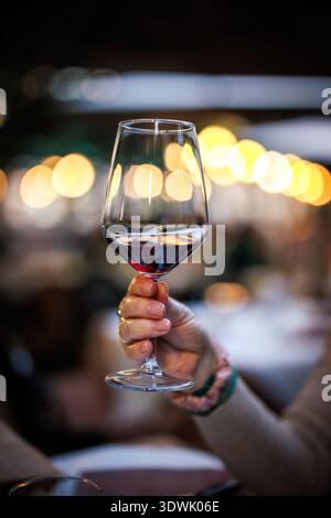Brindisi celebrativo con vino rosso. Donna che tiene in mano la wineglass al ristorante durante la cena. Bere alcolici al bar Foto Stock