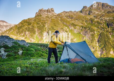 Tenda per escursionisti in montagna. Uomo che prepara una tenda da campeggio ultraleggera durante il viaggio di trekking. Concetto di sopravvivenza all'aperto e stile di vita alpino Foto Stock