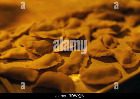 Decine di gnocchi di impasto crudi sono disposti su una superficie piana sotto un caldo bagliore giallo. Foto Stock