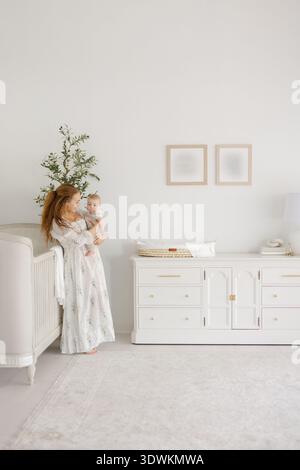 Madre di razza mista che tiene il bambino in un vivaio bianco Foto Stock