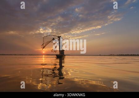 Silhouette di due pescatori in una barca da pesca che lancia una rete da pesca all'alba, in Thailandia Foto Stock