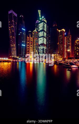 Ammira la terra dei grattacieli illuminati e degli yacht ormeggiati nel porticciolo di Dubai di notte, Dubai, Emirati Arabi Uniti Foto Stock