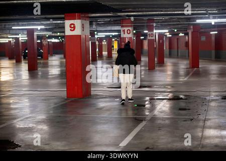 Donna che cammina con una borsa della spesa in un garage sotterraneo vuoto con colonne rosse Foto Stock