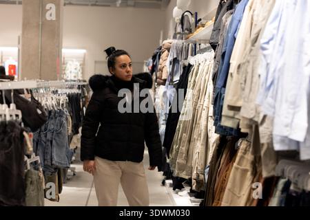 Donna che guarda i portapacchi mentre sfoglia l'abbigliamento in un negozio moderno Foto Stock