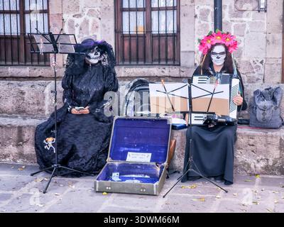 Due donne vestite con costumi in bianco e nero che suonano strumenti. Una delle donne indossa una maschera per il cranio Foto Stock